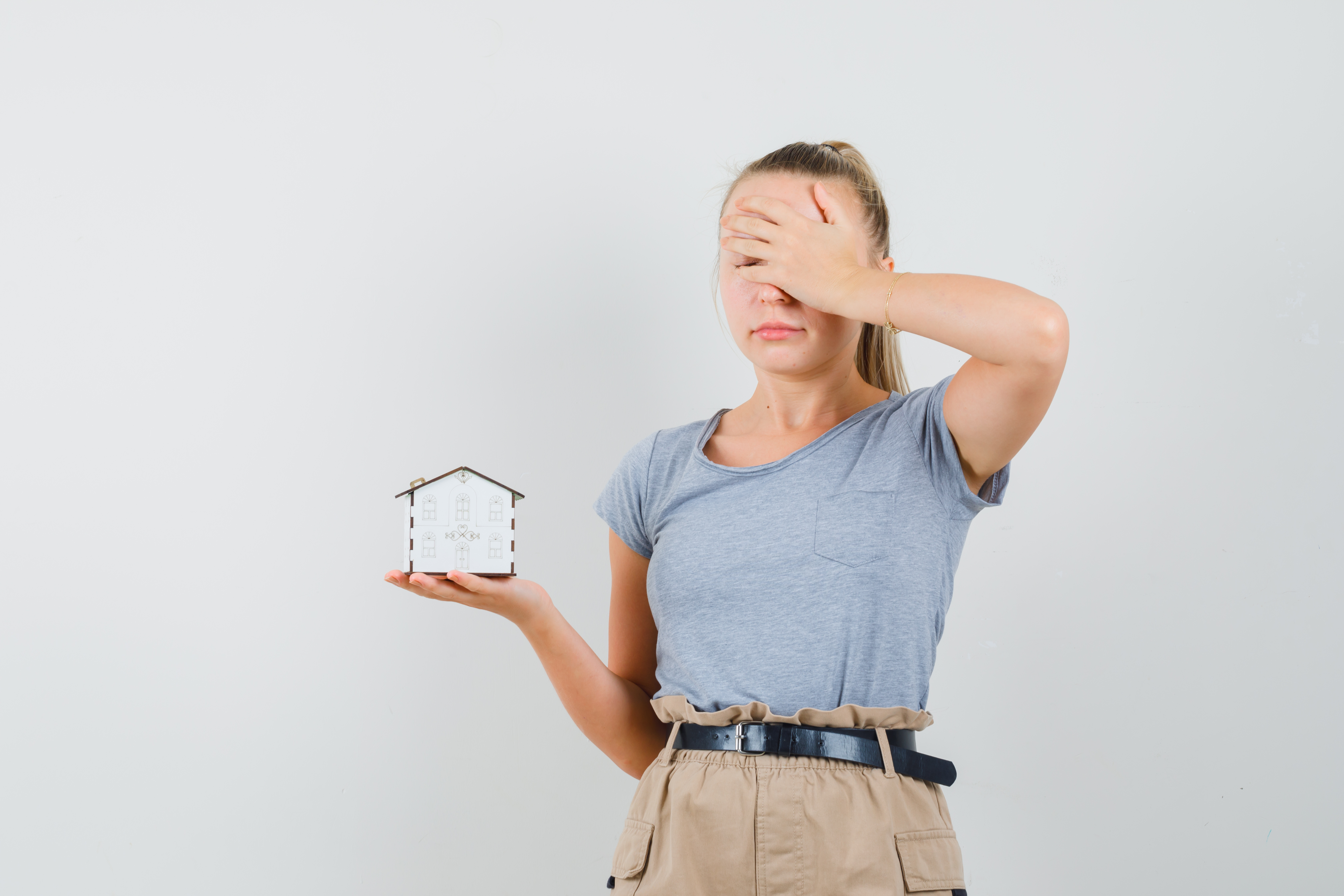 Mujer que se tapa los ojos mientras sostiene una maqueta de una vivienda